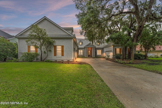 view of front of house featuring driveway, a yard, an attached garage, and stucco siding