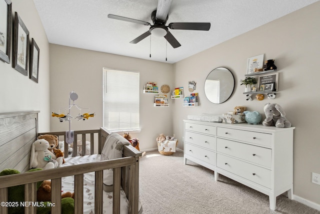 bedroom with light colored carpet, a crib, baseboards, a ceiling fan, and a textured ceiling