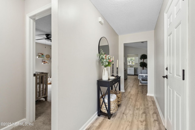 hallway with baseboards, light wood finished floors, and a textured ceiling