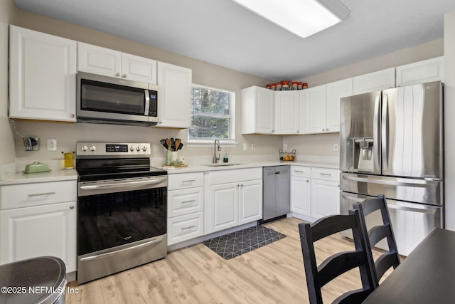 kitchen with stainless steel appliances, a sink, light wood-style floors, white cabinetry, and light countertops