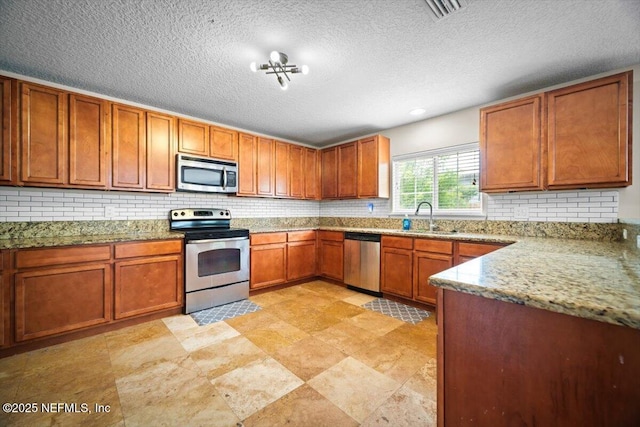 12198 Pebble Point Dr S, Jacksonville, FL 32218 - kitchen with stainless steel appliances, a sink, tasteful backsplash, brown cabinets, and light stone counters