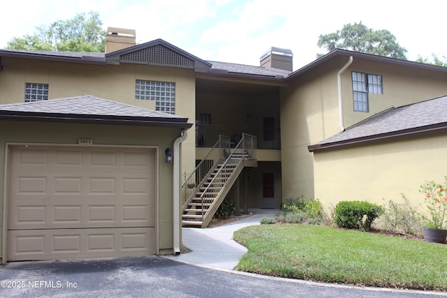 view of front of property with a chimney, stucco siding, stairs, driveway, and roof with shingles