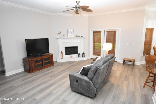 living room with ceiling fan, crown molding, french doors, light wood-style floors, and a tiled fireplace