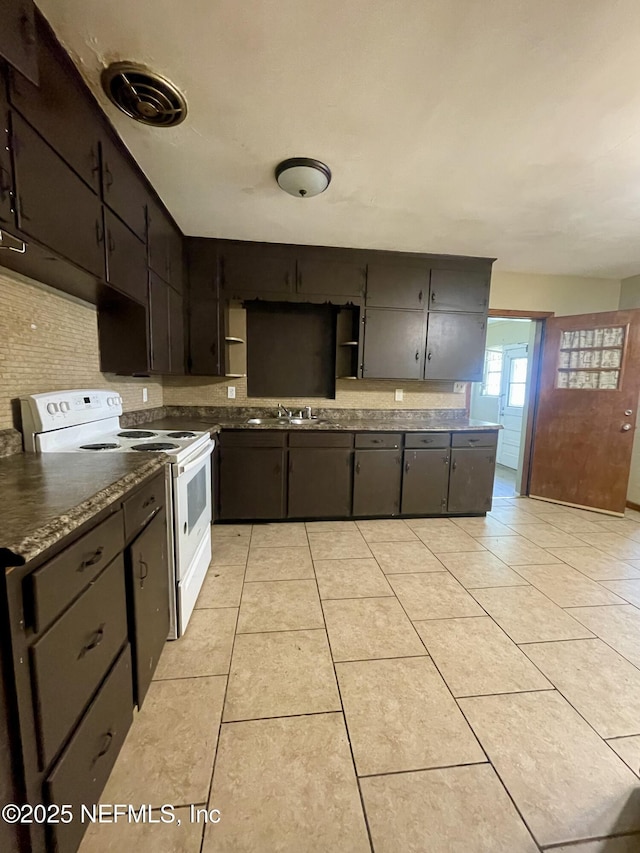 kitchen with white electric range, light tile patterned flooring, dark countertops, open shelves, and a sink