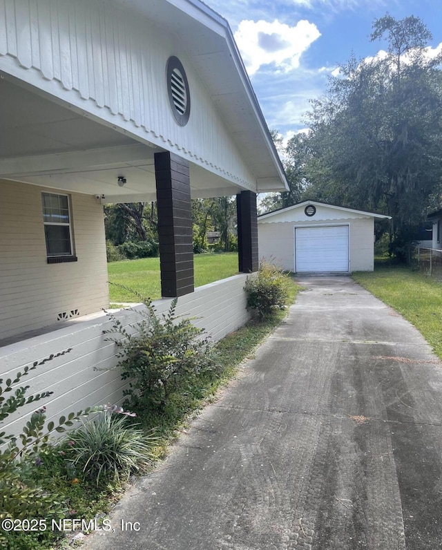 view of side of property with an outbuilding, asphalt driveway, a detached garage, and a lawn