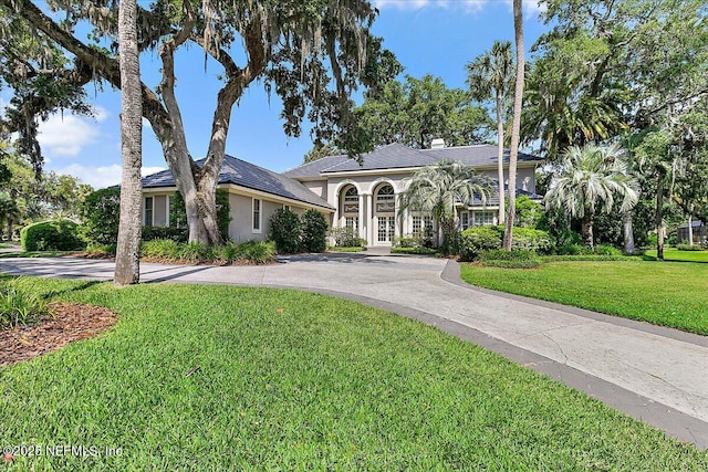 view of front facade featuring curved driveway, a front yard, stucco siding, and a chimney