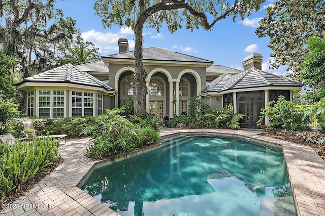 rear view of property with french doors, a chimney, a patio, stucco siding, and an outdoor pool