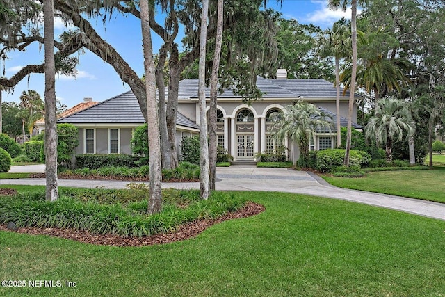 view of front of house with french doors, a chimney, curved driveway, stucco siding, and a front yard