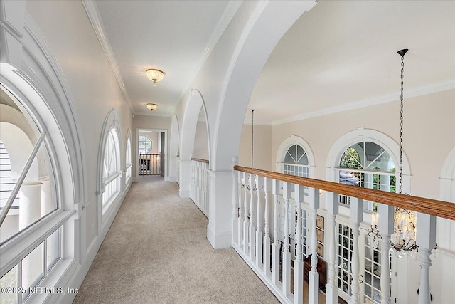 hallway with light colored carpet, ornamental molding, and arched walkways