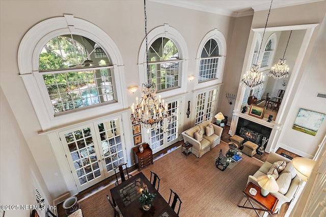 living room with a chandelier, french doors, a towering ceiling, crown molding, and wood finished floors
