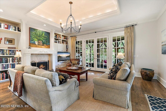 living room featuring a tray ceiling, a chandelier, a lit fireplace, built in features, and ornamental molding