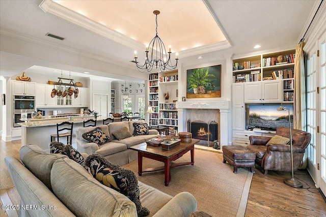 living room featuring a tray ceiling, crown molding, a chandelier, light wood finished floors, and healthy amount of natural light