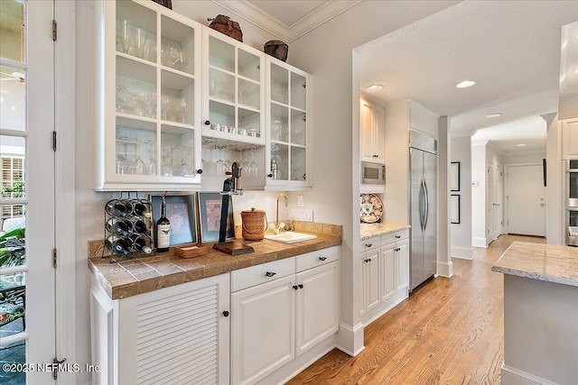 indoor wet bar with built in appliances, ornamental molding, light wood finished floors, recessed lighting, and baseboards