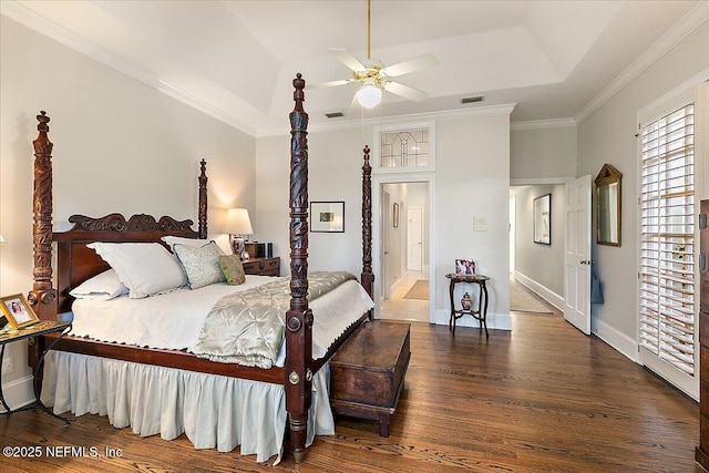 bedroom featuring wood finished floors, a tray ceiling, crown molding, ceiling fan, and baseboards