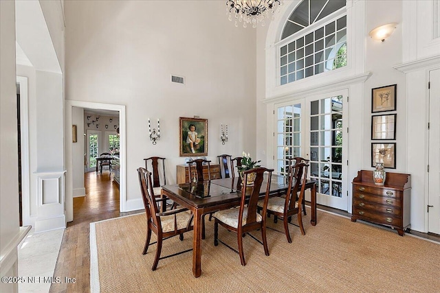 dining space featuring french doors, a high ceiling, light wood-style flooring, and a chandelier