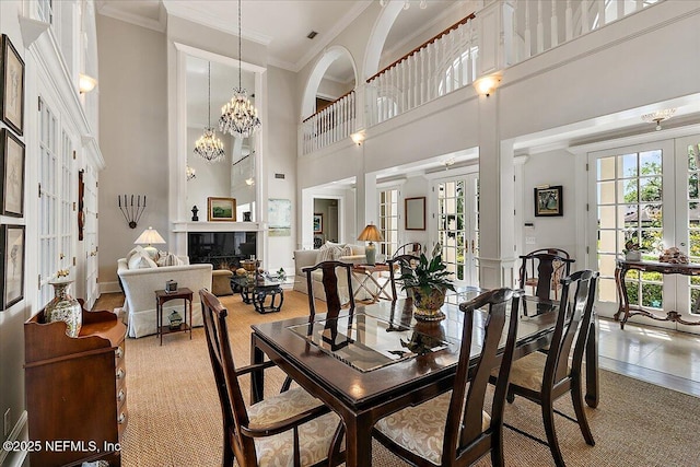 dining area featuring french doors, ornamental molding, a high ceiling, a premium fireplace, and a chandelier