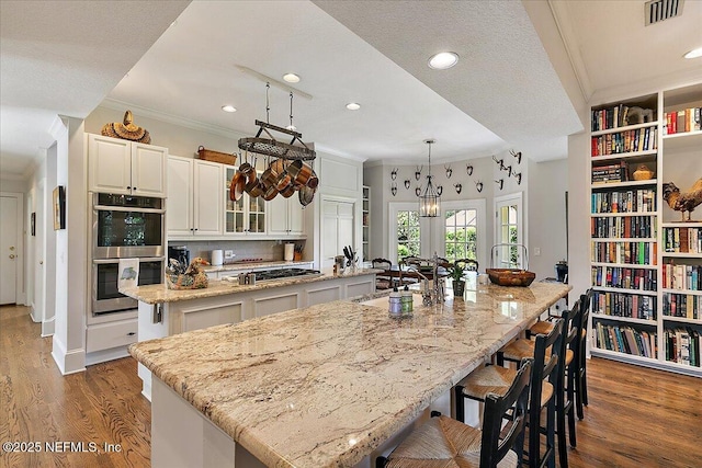kitchen with stainless steel appliances, a large island with sink, ornamental molding, wood finished floors, and a kitchen bar