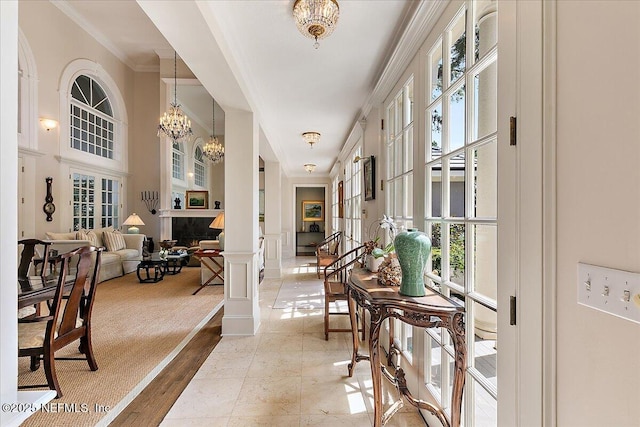 hall featuring plenty of natural light, ornamental molding, a chandelier, and decorative columns