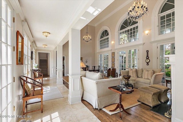 living room featuring a chandelier, french doors, crown molding, a towering ceiling, and a wainscoted wall
