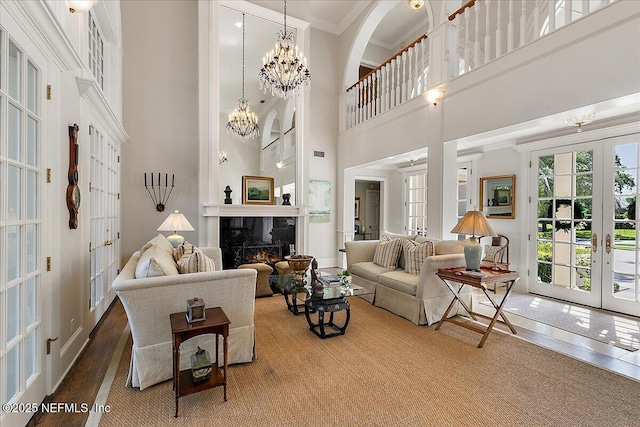 living room with french doors, a high ceiling, ornamental molding, a high end fireplace, and a chandelier