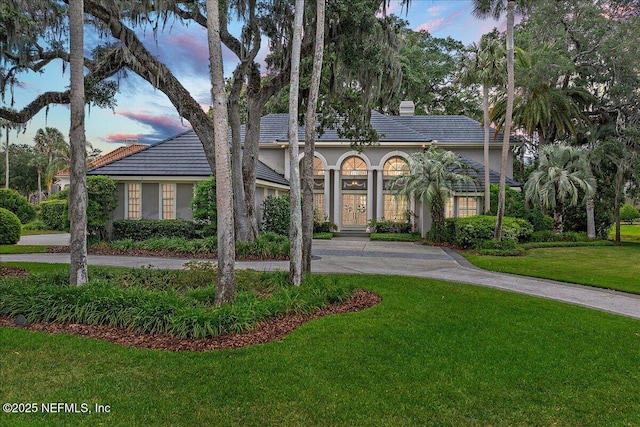 view of front facade with curved driveway, a lawn, stucco siding, and a chimney
