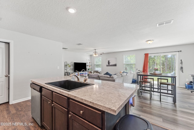kitchen with a sink, stainless steel dishwasher, light countertops, dark wood-style flooring, and a textured ceiling
