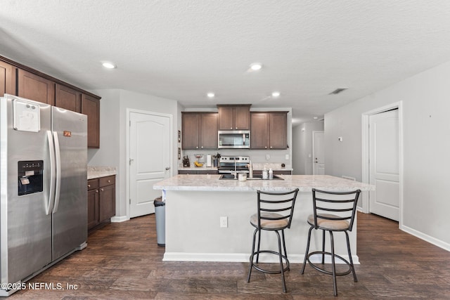 kitchen with stainless steel appliances, dark wood-style floors, an island with sink, dark brown cabinetry, and recessed lighting
