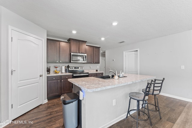 kitchen featuring appliances with stainless steel finishes, a sink, dark wood-type flooring, an island with sink, and light countertops