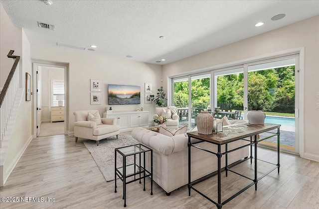 living area with light wood finished floors, stairs, baseboards, healthy amount of natural light, and a textured ceiling