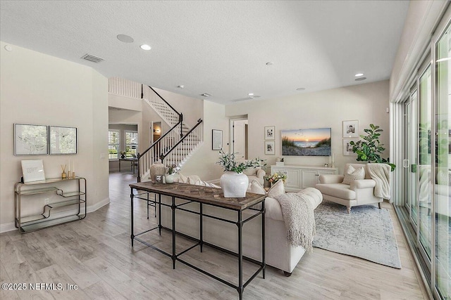 living area with light wood-type flooring, stairs, recessed lighting, baseboards, and a textured ceiling