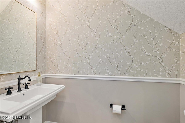 bathroom featuring a sink, wallpapered walls, and a textured ceiling