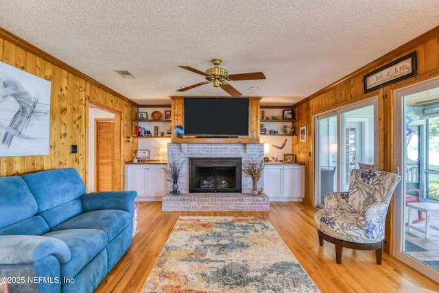 130 Woodbury Trl, Satsuma, FL 32189 - living area with crown molding, wooden walls, a ceiling fan, light wood-style flooring, and a brick fireplace