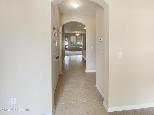 hall featuring arched walkways, light tile patterned floors, and baseboards