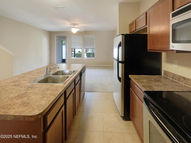 kitchen featuring stainless steel appliances, a sink, brown cabinetry, open floor plan, and light colored carpet