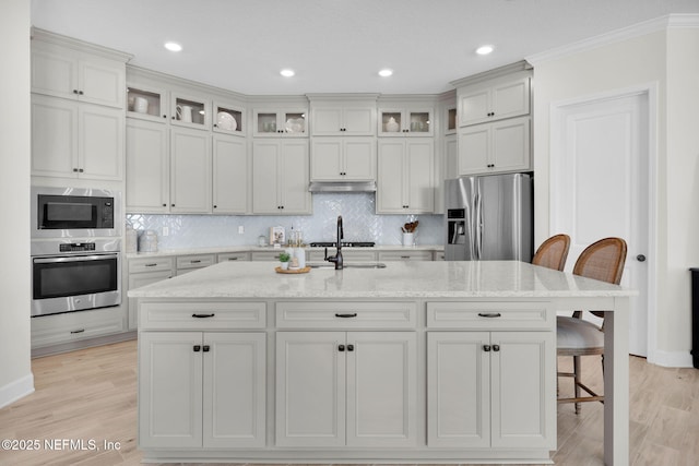 111 Bucktail Ave, Ponte Vedra, FL 32081 - kitchen featuring appliances with stainless steel finishes, under cabinet range hood, a breakfast bar area, light wood finished floors, and tasteful backsplash