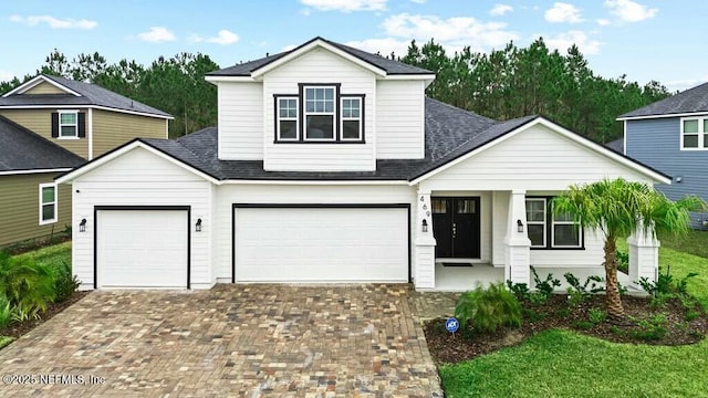 traditional home with a porch, roof with shingles, decorative driveway, and a garage