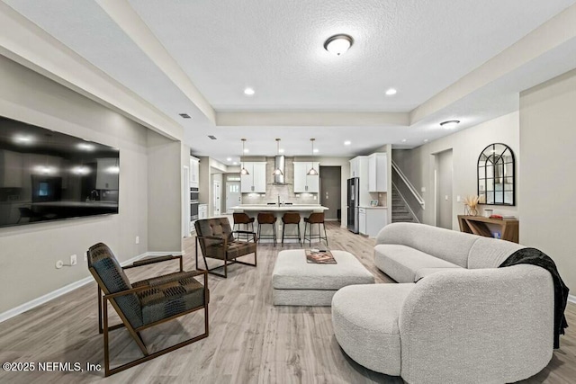 living room featuring light wood-style flooring, stairway, baseboards, a textured ceiling, and a raised ceiling