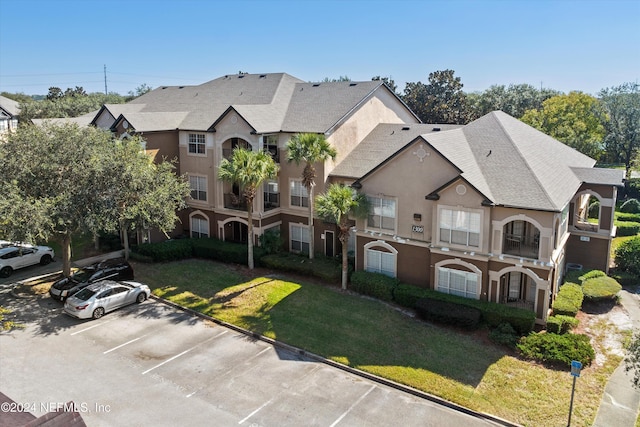 10961 Burnt Mill Rd Unit 1311, Jacksonville, FL 32256 - view of front of home with uncovered parking, stucco siding, a front lawn, and a shingled roof