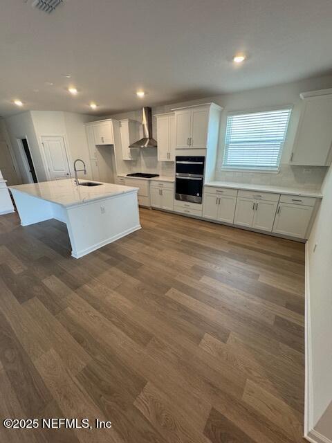 317 Archstone Way, Saint Augustine, FL 32092 - kitchen with wall chimney range hood, dark wood-style flooring, stovetop, an island with sink, and recessed lighting