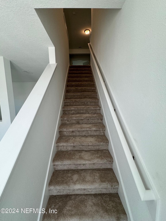 staircase featuring carpet flooring and a textured ceiling