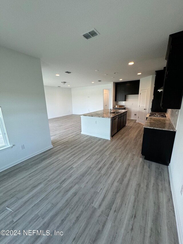kitchen with open floor plan, stone counters, light wood-style flooring, dark cabinets, and recessed lighting