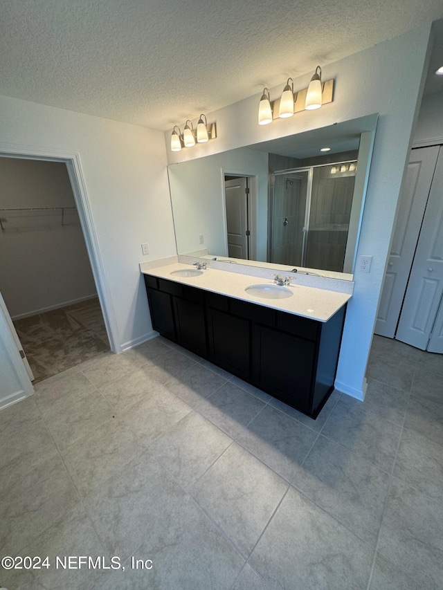 full bath with a shower stall, a textured ceiling, double vanity, a walk in closet, and baseboards