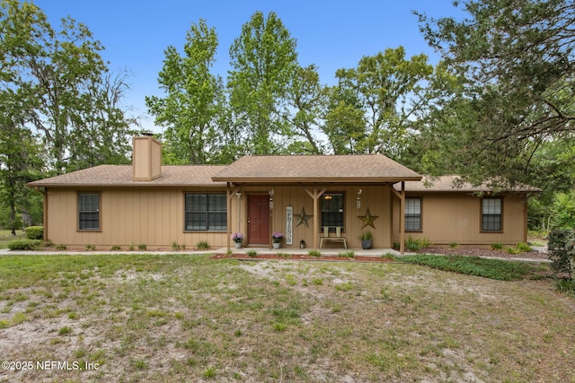 ranch-style home with a porch, a chimney, and a front yard