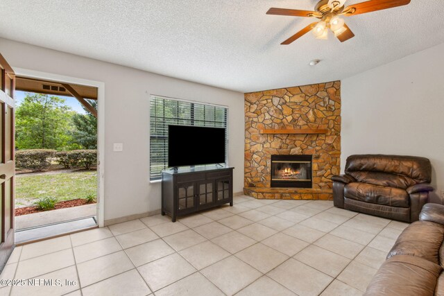 living area featuring ceiling fan, a textured ceiling, a stone fireplace, and light tile patterned floors