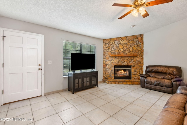 living room with a ceiling fan, a textured ceiling, a stone fireplace, and light tile patterned floors