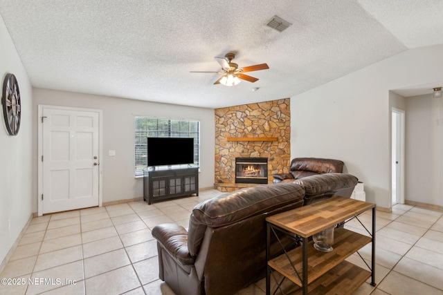 living area with ceiling fan, light tile patterned floors, a stone fireplace, lofted ceiling, and a textured ceiling