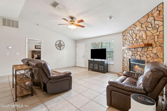 living area with lofted ceiling, a fireplace, ceiling fan, light tile patterned flooring, and a textured ceiling