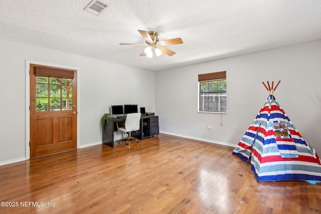 bedroom with multiple windows, wood finished floors, a textured ceiling, an office area, and ceiling fan