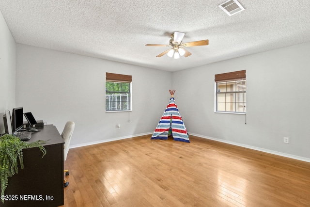 recreation room with ceiling fan, light wood-style floors, baseboards, a desk, and a textured ceiling