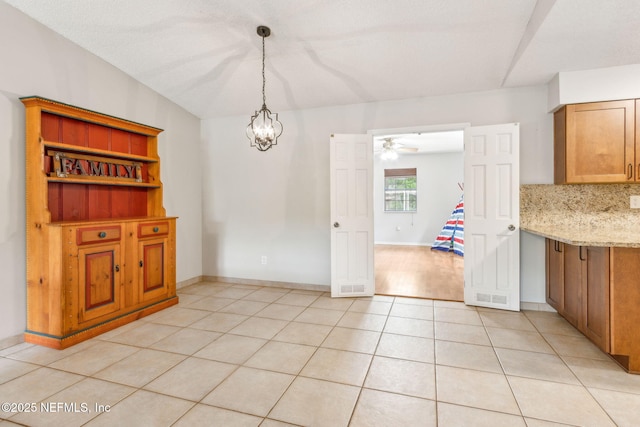 unfurnished dining area with light tile patterned floors, ceiling fan, a chandelier, and baseboards